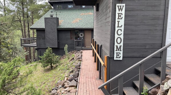 Un bâtiment moderne, agrémenté d’une enseigne « BIENVENUE », d’une terrasse en bois et d’un chemin de pierre menant à l’entrée.