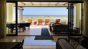 An open-plan living area with a view of the sea, furnished with sofas, chairs, and a dining table.