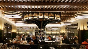 A restaurant with a bar area, wooden ceiling beams, and hanging circular chandeliers.