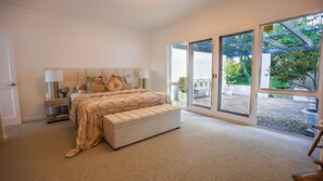 A bedroom with a large bed, a nightstand, a bench, and a view of the outdoors through large sliding doors. - Southern Highlands Finest! (Exeter)