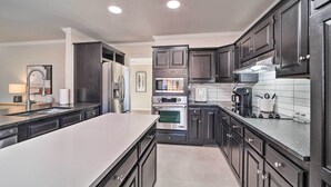 A modern kitchen with dark cabinetry, stainless steel appliances, and a large island. - Immaculate 'Woodland View' Retreat w/ Hot Tub (Tulsa)