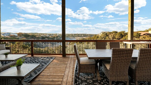 Eine Holzterrasse mit Gartenmöbeln, Geländer und Blick auf eine Landschaft mit Bäumen und Gebäuden.