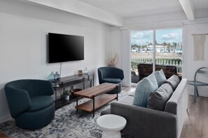 Una sala de estar moderna con una televisión de pantalla plana, dos sillones, un sofá, una mesa de centro y vistas a barcos a través de amplios ventanales.