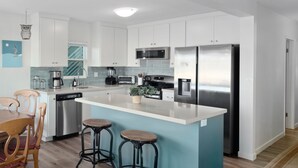 Een moderne keuken met witte kasten, roestvrijstalen apparatuur, een centraal eiland met krukken en een eethoek met houten stoelen.