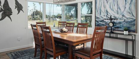 A dining area with a wooden table, six chairs, and a large window with a view of palm trees.