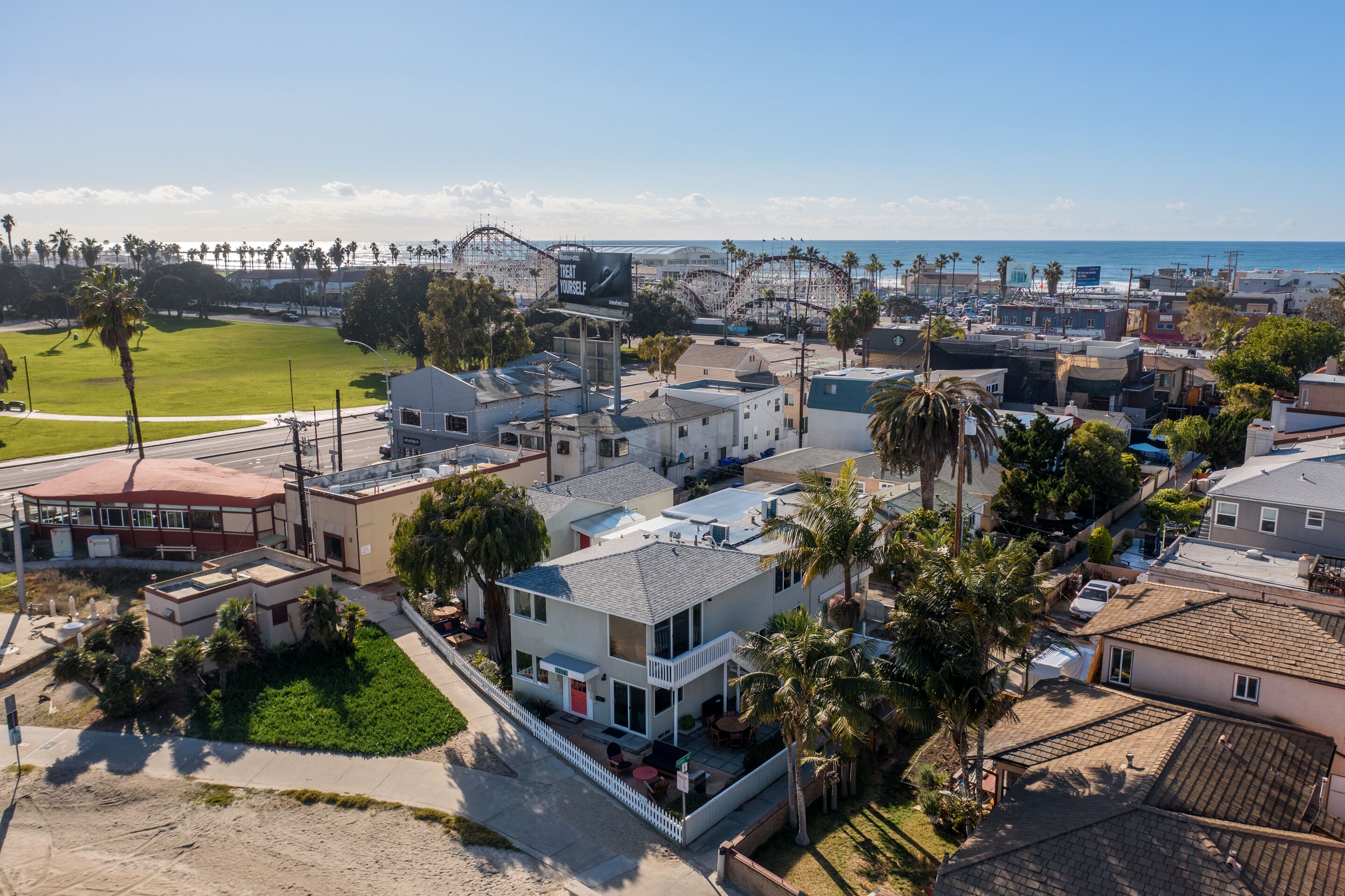 A coastal residential area with a mix of single and multi-story houses, some with balconies, and a visible amusement park in the background.