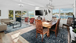 A modern living room with a large dining table, comfortable seating, a flat-screen TV, and a view of the marina. - Waterfront Condo | AC | Beach Toys | Walk to All! (San Diego)