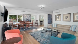 A spacious living area with a dining table, sofas, and a coffee table. There is a kitchen in the background, and artwork is displayed on the walls. - Waterfront Condo | AC | Beach Toys | Walk to All! (San Diego)
