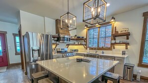 A modern kitchen with a large island, stainless steel appliances, and wooden accents. - New Construction Lakefront Home with Private Dock, Fire Pit, Hot Tub (Swanton)
