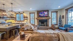 A spacious living area with a fireplace, a large TV mounted above it, and a cozy seating arrangement. - New Construction Lakefront Home with Private Dock, Fire Pit, Hot Tub (Swanton)