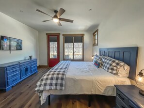 A bedroom with a bed, a ceiling fan, a TV, a dresser, and a window with a view. - New Construction Lakefront Home with Private Dock, Fire Pit, Hot Tub (Swanton)