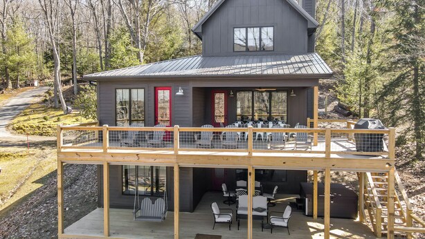 A two-story cabin with a balcony, outdoor seating area, and a fireplace. - New Construction Lakefront Home with Private Dock, Fire Pit, Hot Tub (Swanton)