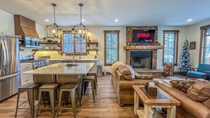 A modern kitchen with a central island, bar stools, and a fireplace. - New Construction Lakefront Home with Private Dock, Fire Pit, Hot Tub (Swanton)