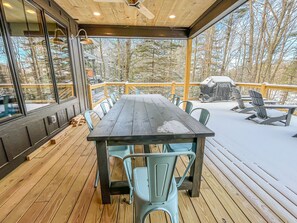 A wooden deck with a table and chairs, a covered grill, and a view of trees. - New Construction Lakefront Home with Private Dock, Fire Pit, Hot Tub (Swanton)