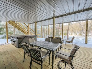 A covered outdoor deck with a table and chairs, a grill, and a staircase leading to an upper level. - New Construction Lakefront Home with Private Dock, Fire Pit, Hot Tub (Swanton)