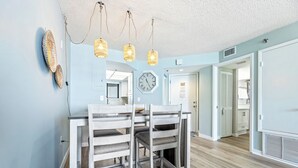 A dining area with a wooden table and chairs, a clock on the wall, and pendant lights.