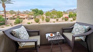 Un balcon avec deux fauteuils en osier, une petite table et une vue sur un quartier résidentiel avec des maisons et des arbres.
