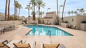Un espace piscine avec des chaises longues, des palmiers et un bâtiment doté d’un toit plat.