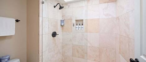 A shower with a skylight, a toilet, and a small shelf with toiletries.