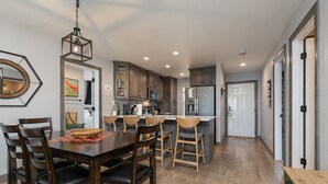 A modern kitchen with wooden cabinets, a central island, and a dining area with dark wooden chairs and a table. - Game-Time Getaway 3BR Family Condo w/ 3 baths + Patio | Champions 3-2 (Branson)