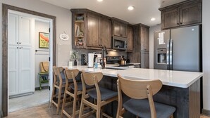 A modern kitchen with wooden cabinets, a stainless steel refrigerator, and a central island with bar stools. - Game-Time Getaway 3BR Family Condo w/ 3 baths + Patio | Champions 3-2 (Branson)