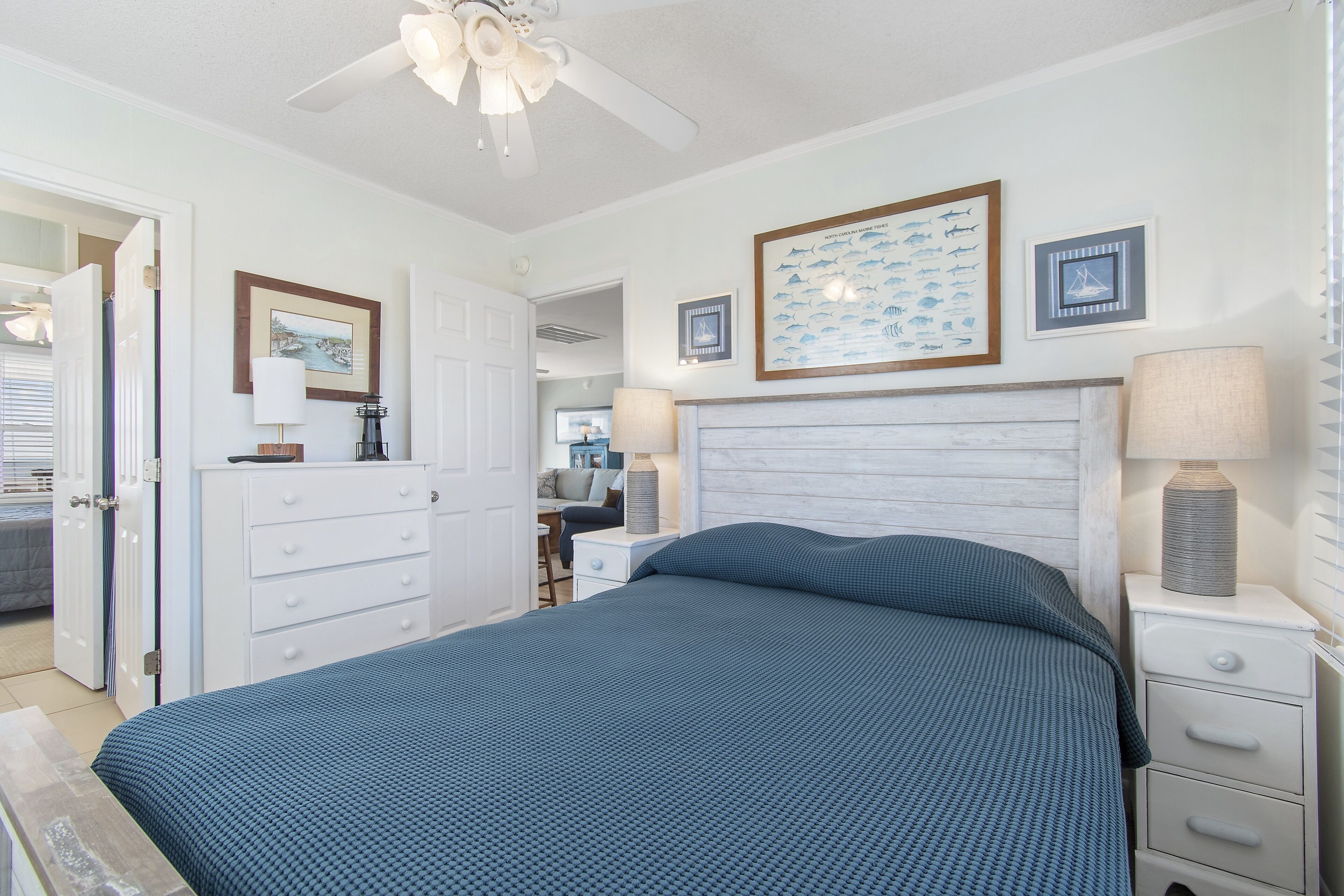 A bedroom with a bed, a nightstand, a dresser, a ceiling fan, and wall art.