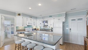 Una cocina amplia con una isla grande, armarios blancos y una barra de desayuno con taburetes.