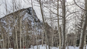 A hot tub with a wooden exterior and a brown cover, surrounded by snow-covered ground and leafless trees. - Modern Mountain Retreat in Frisco: Hot Tub, Fireplace, Views, Near Everything! (Frisco)