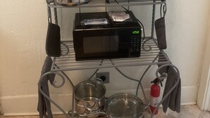 Une cuisine équipée d’une étagère en métal où sont rangées des casseroles, des poêles, un grille-pain et un four à micro-ondes.