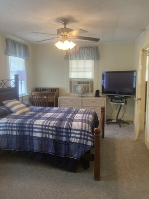 Une chambre à coucher comprenant un lit, un bureau, une chaise, un téléviseur et un ventilateur de plafond.