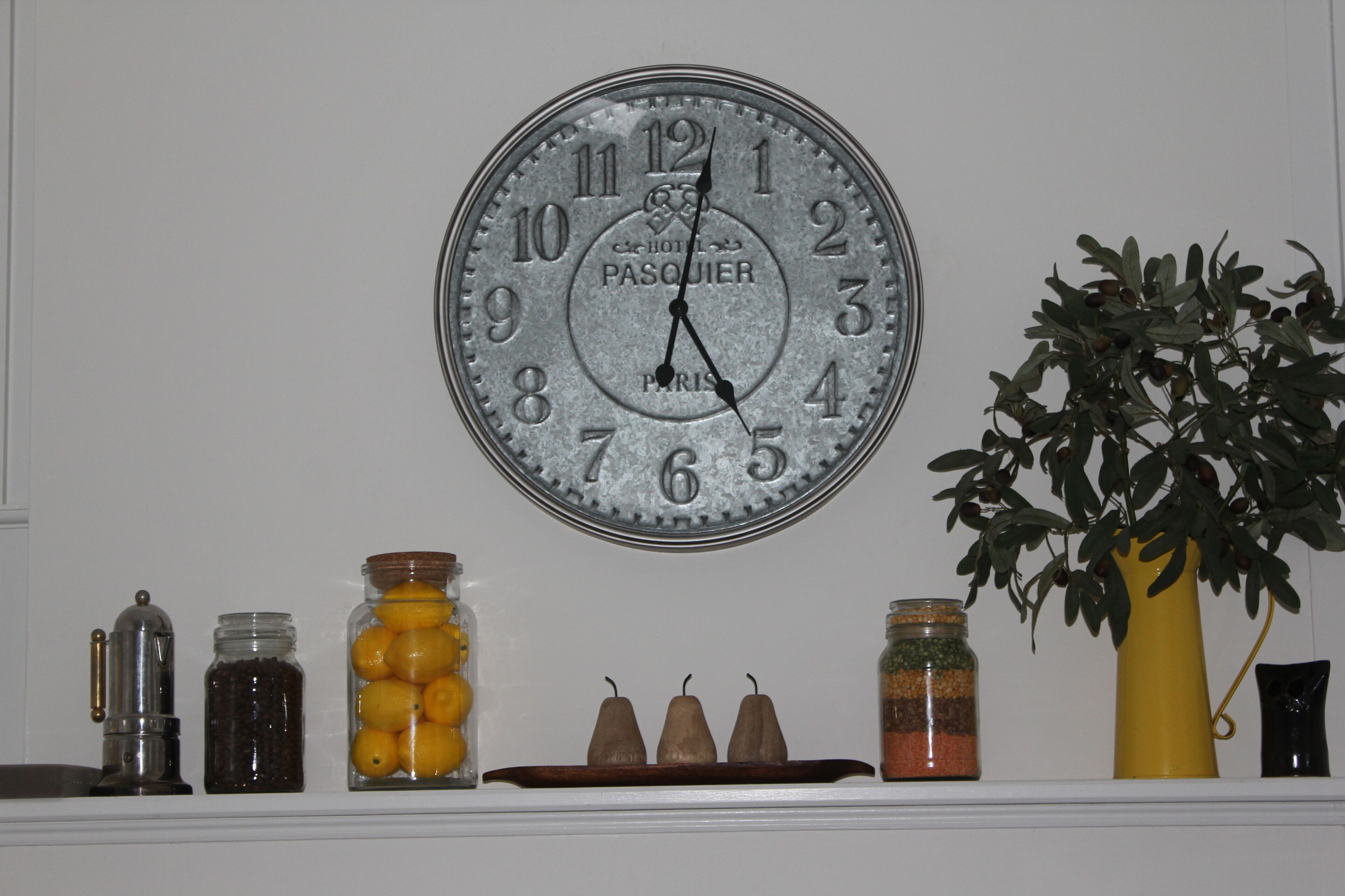 Une horloge murale dotée d’un cadre métallique et d’un cadran blanc, entourée de divers objets décoratifs placés sur une étagère.