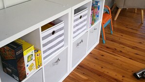 A white storage unit with multiple drawers and shelves, wooden flooring, and a grey chair in the background. - Merala: cosy cottage with an easy stroll to CBD (Mudgee)
