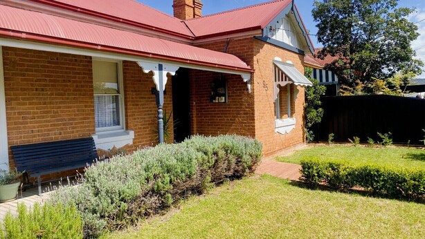 A brick house with a red roof, a front porch, and a well-maintained garden. - Merala: cosy cottage with an easy stroll to CBD (Mudgee)