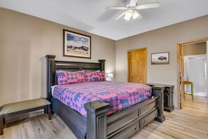 Een slaapkamer met een bed, een bankje, een plafondventilator, een deur en een ingelijst schilderij aan de muur.
