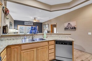 A kitchen with a granite countertop, wooden cabinets, a dishwasher, and a ceiling fan. - Prime Lake Access Retreat with Stunning Views, Free WiFi, Private Grill & Free Daily Tickets! (Branson)
