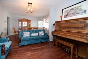 Relax in this stylish living room with a plush sofa, wooden piano, and dining area.