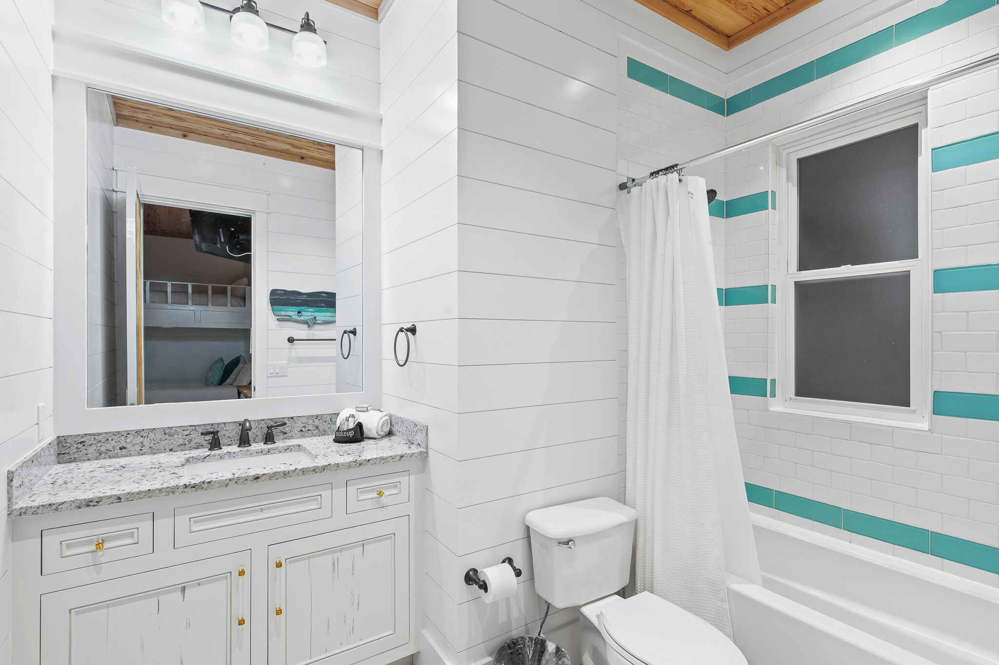 A bathroom with white tiled walls, a shower with a window, a sink with a mirror, and a toilet.