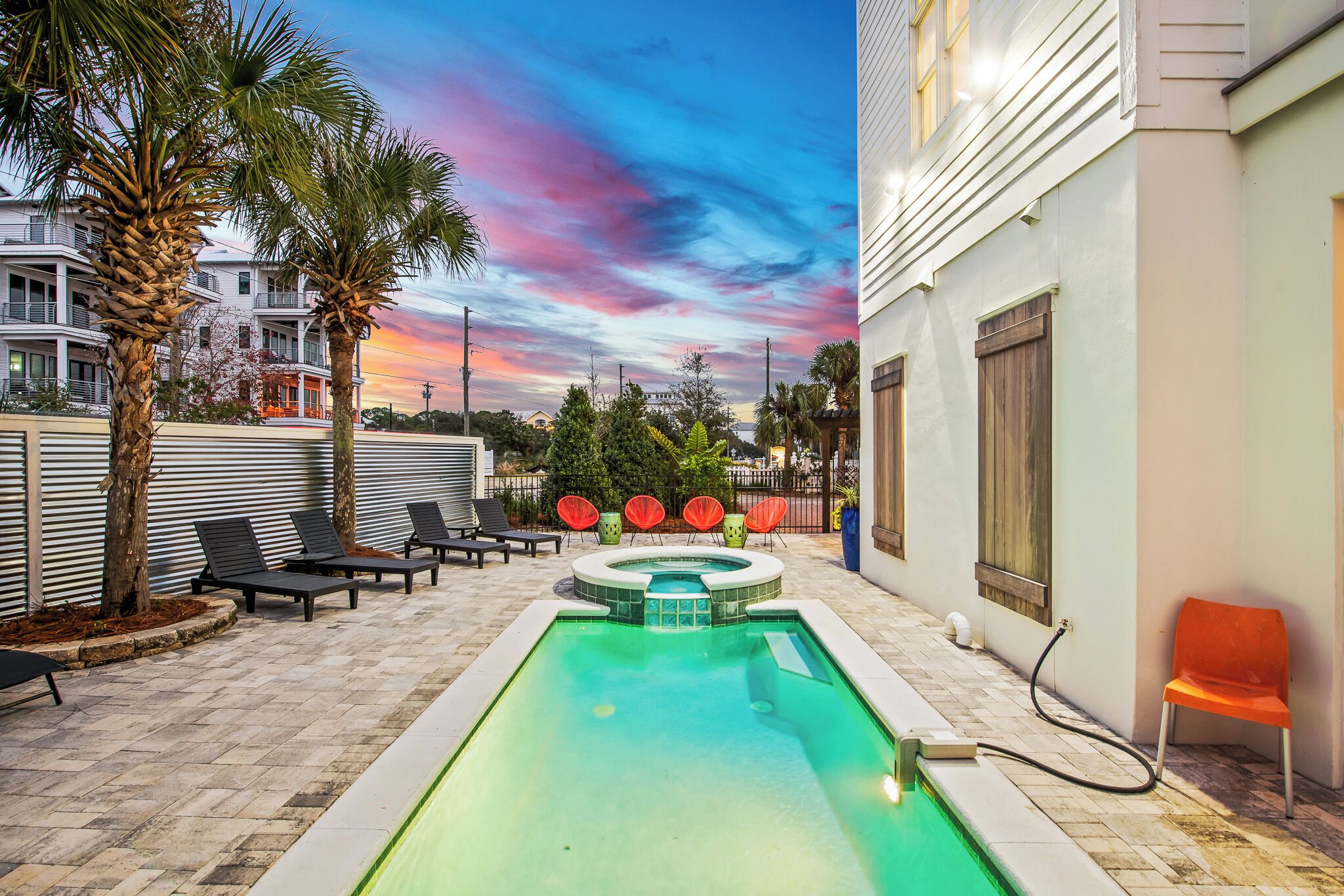 A swimming pool with lounge chairs and a hot tub, surrounded by palm trees and a sunset view.