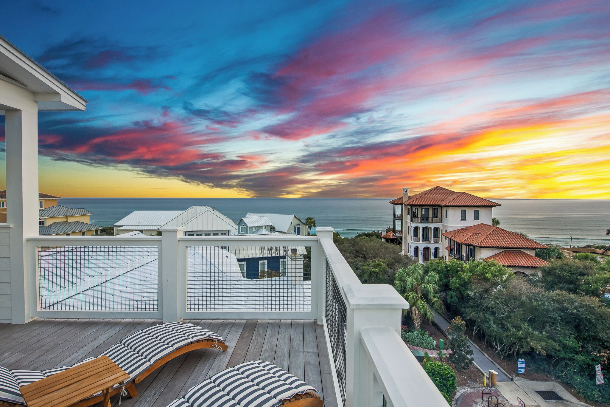A balcony with wooden lounge chairs and a view of the ocean during sunset.