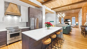 A modern kitchen with a large island, stainless steel appliances, and wooden ceiling beams. - 12 Periwinkle Ln - Beach Blessings (Santa Rosa Beach)