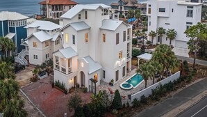 A large white house with a swimming pool, surrounded by palm trees and a view of the ocean. - 12 Periwinkle Ln - Beach Blessings (Santa Rosa Beach)