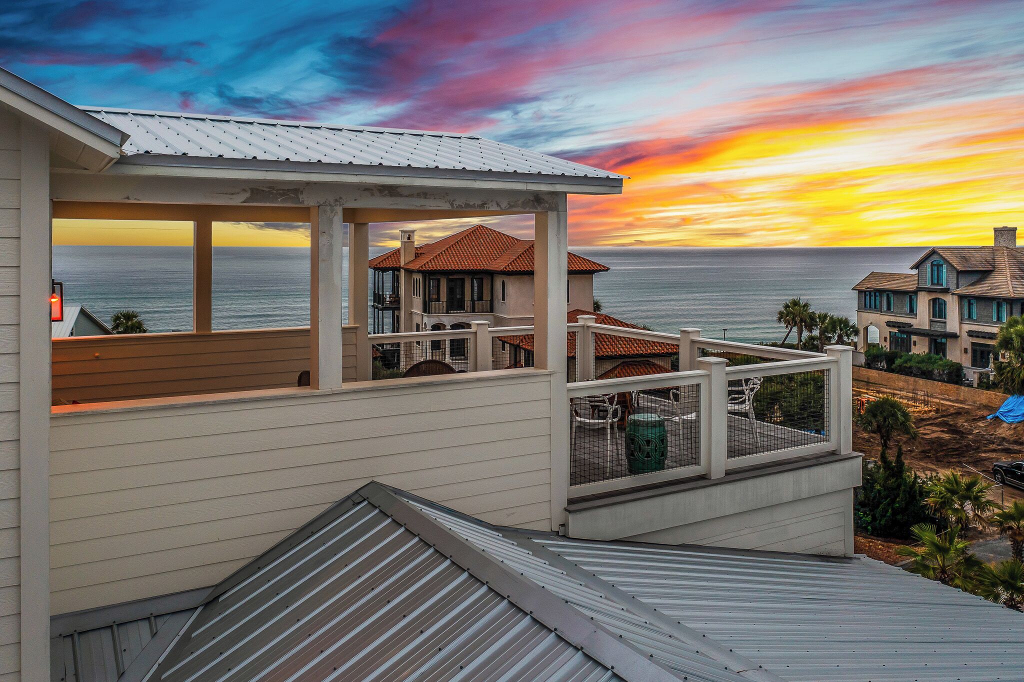 A coastal house with a balcony overlooking the ocean, featuring a view of the sunset.