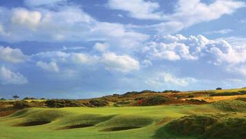 A golf course with rolling hills, a red flag marking the hole, and a clear sky.