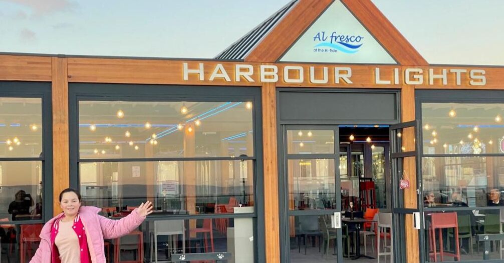 Een restaurant genaamd 'Harbour Lights' met een modern design, met grote ramen en een zichtbaar interieur met tafels en stoelen.