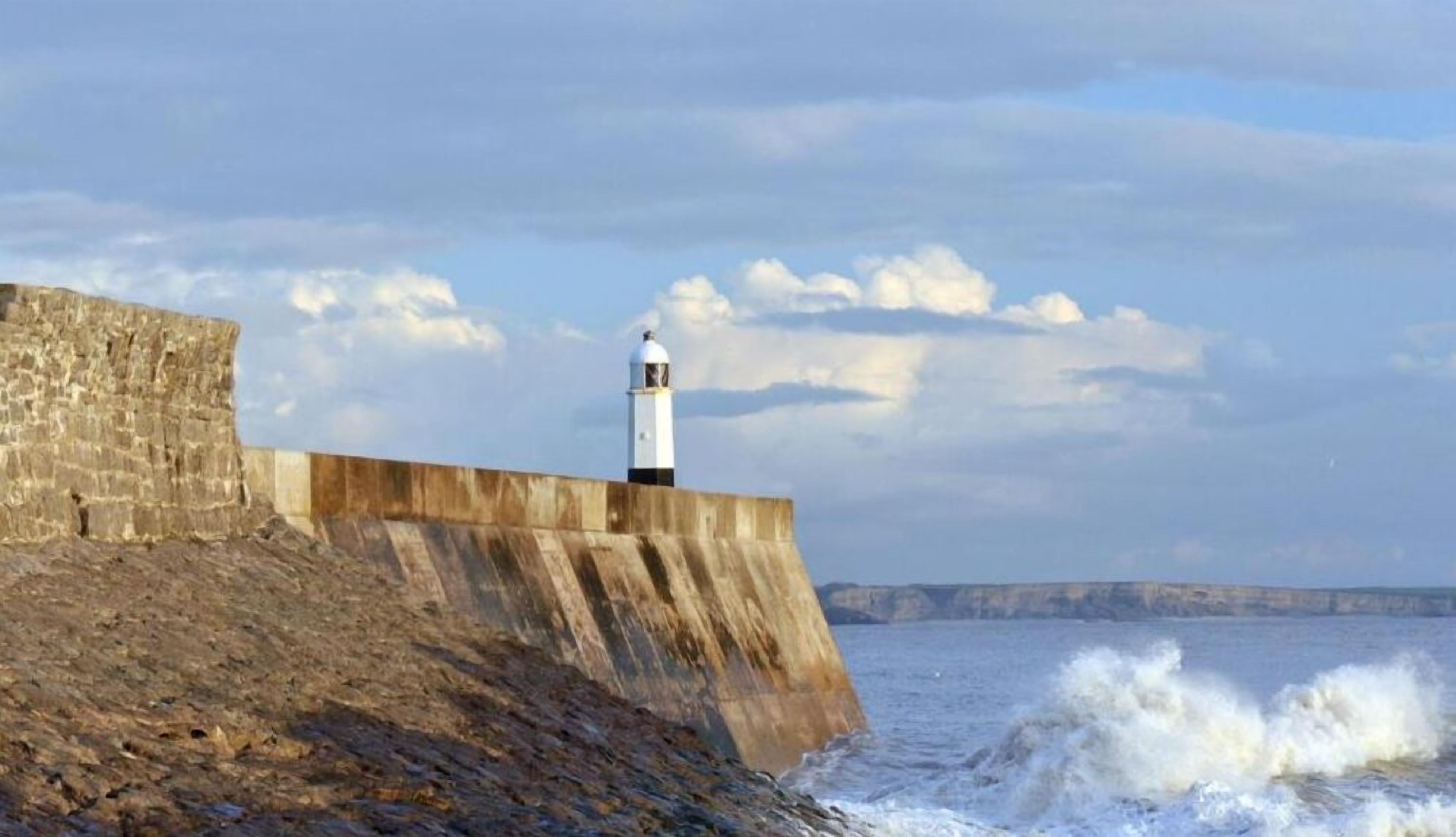 Un faro sobre una estructura de concreto a la orilla del mar, con olas rompiendo debajo.