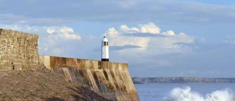 Un faro sobre una estructura de concreto a la orilla del mar, con olas rompiendo debajo.