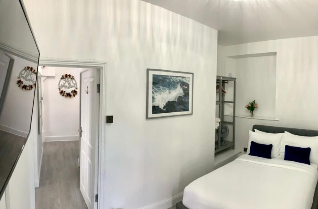 Ein Schlafzimmer mit einem Bett, einem gerahmten Bild, einem Spiegel und einer Tür zu einem anderen Raum.