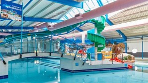 Ein Hallenbad mit deutlich markierten Bahnen, einer Wasserrutsche und einem Kinderspielbereich.