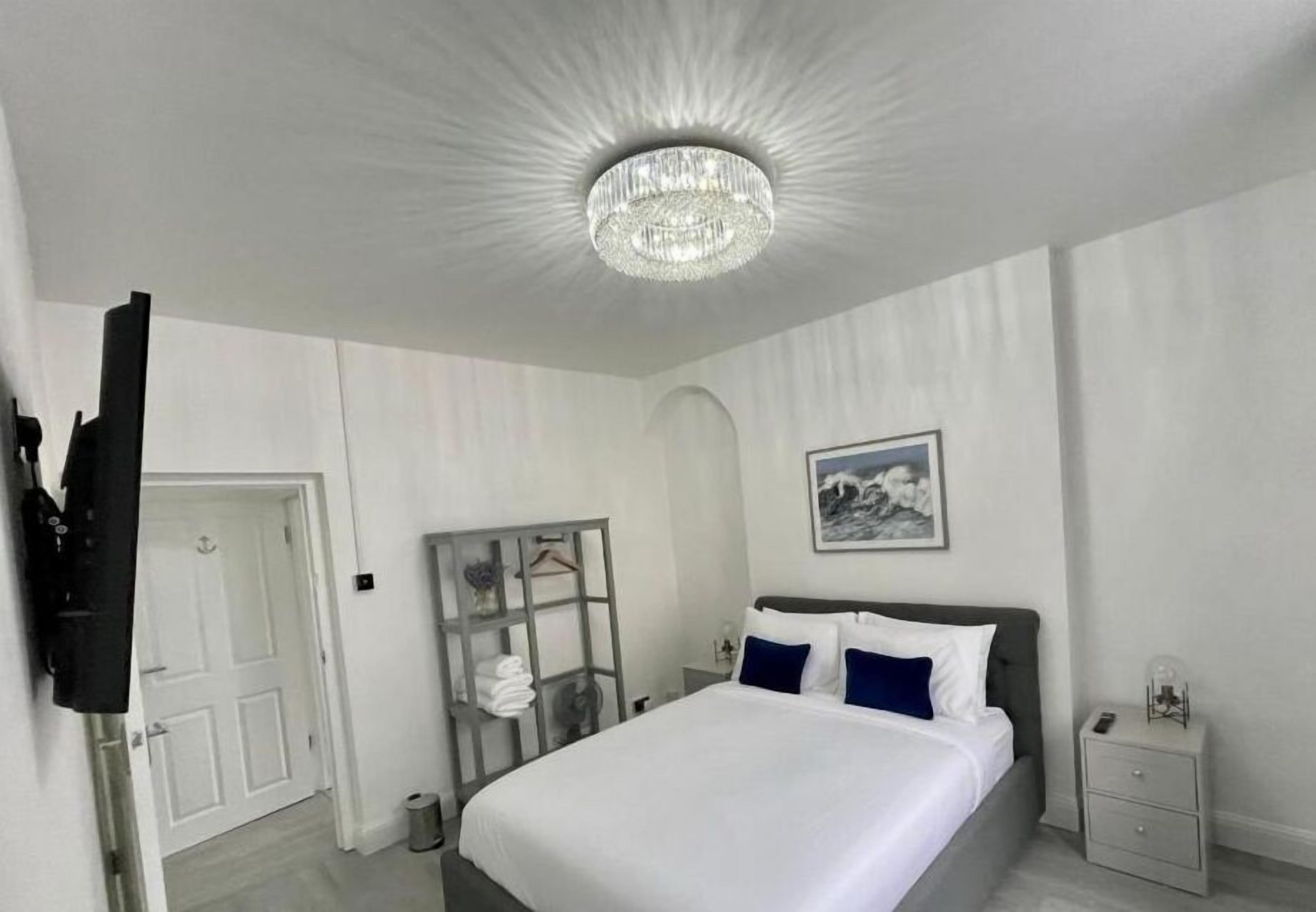 Quarto de hotel com uma cama grande, um candelabro, uma pintura, um guarda-roupa e uma mesa de cabeceira.