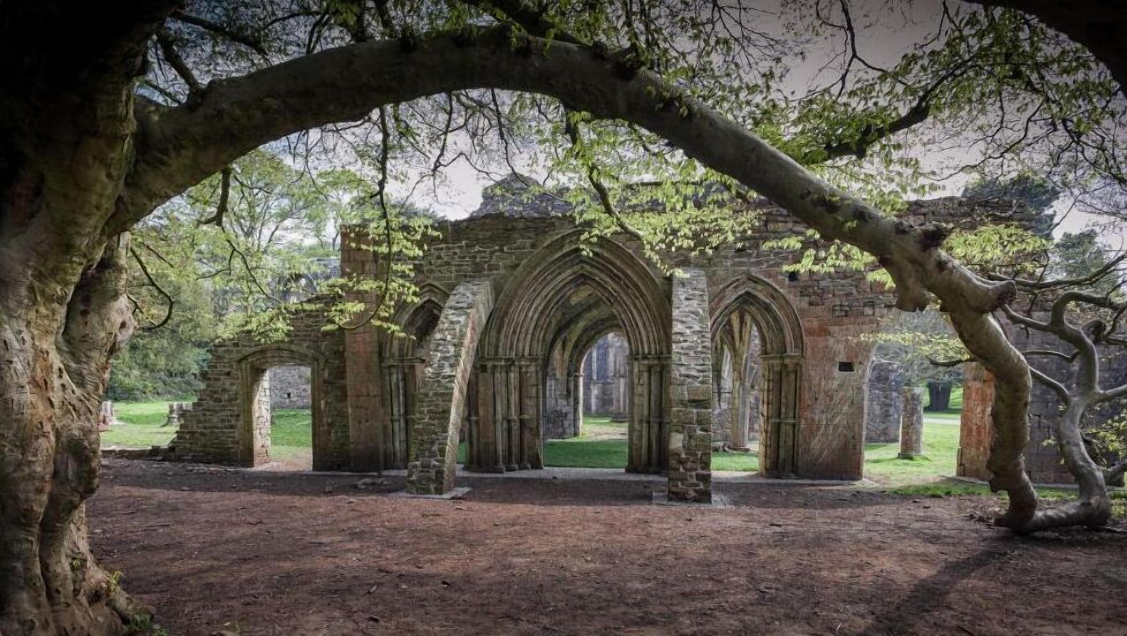 Eine uralte Steinarchitektur mit Bögen und Säulen, umgeben von Bäumen und Gras.